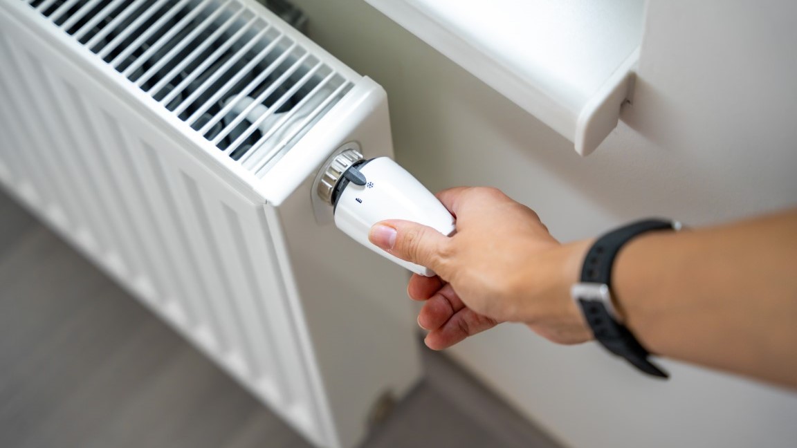 A woman's hand turns the battery heating knob. Heating in an apartment, at home. Heating prices.